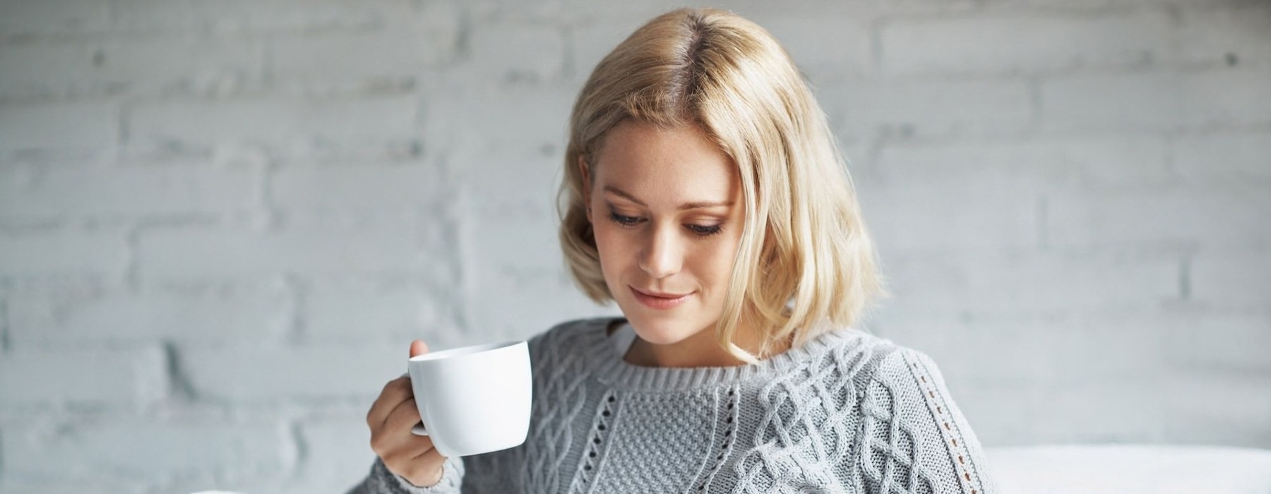 a woman sitting on a couch looking a tablet while holding a mug